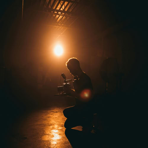 A silhouette of a person crouching on the ground in a dimly lit room with a bright light source in the background.