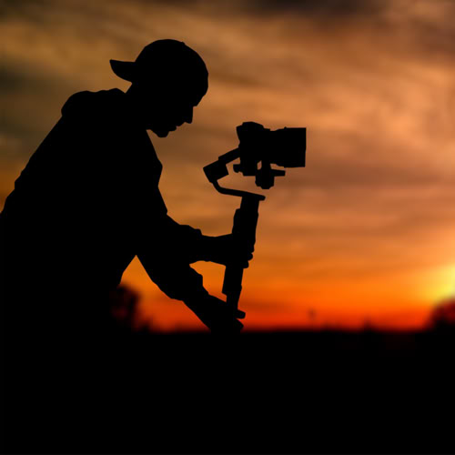 Videographer in silhouette using a camera gimbal at sunset